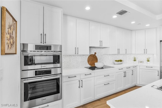 kitchen featuring black electric stovetop, stainless steel double oven, visible vents, white cabinetry, and light countertops