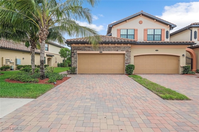 mediterranean / spanish home featuring a garage, stone siding, a tile roof, decorative driveway, and stucco siding