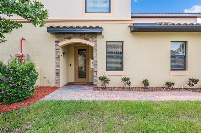 property entrance featuring stone siding, a tiled roof, a yard, and stucco siding