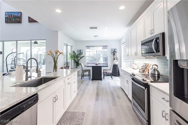 kitchen with visible vents, a sink, stainless steel appliances, light wood-style floors, and decorative backsplash