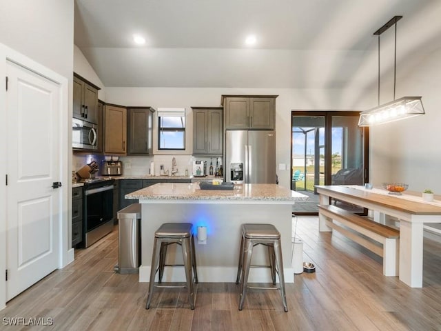509 SW 8th Ct, Cape Coral, FL 33991 - kitchen featuring appliances with stainless steel finishes, a breakfast bar, vaulted ceiling, light stone countertops, and a center island