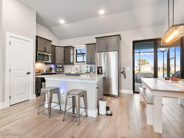 509 SW 8th Ct, Cape Coral, FL 33991 - kitchen featuring appliances with stainless steel finishes, vaulted ceiling, a breakfast bar, light wood-style floors, and dark brown cabinetry