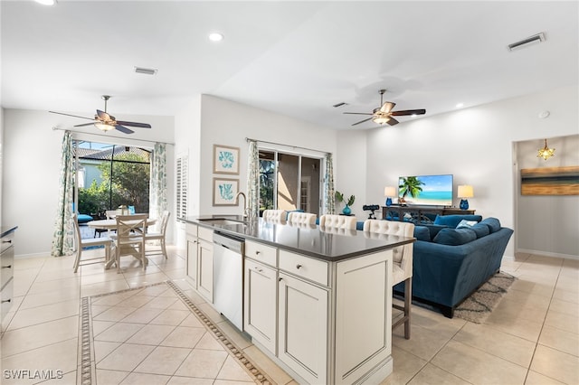 kitchen featuring light tile patterned floors, dark countertops, visible vents, stainless steel dishwasher, and a sink