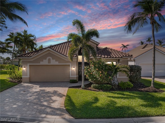 mediterranean / spanish house featuring a front lawn, decorative driveway, an attached garage, and stucco siding