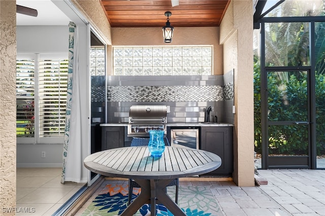 view of patio / terrace featuring outdoor dining area, grilling area, glass enclosure, a sink, and exterior kitchen