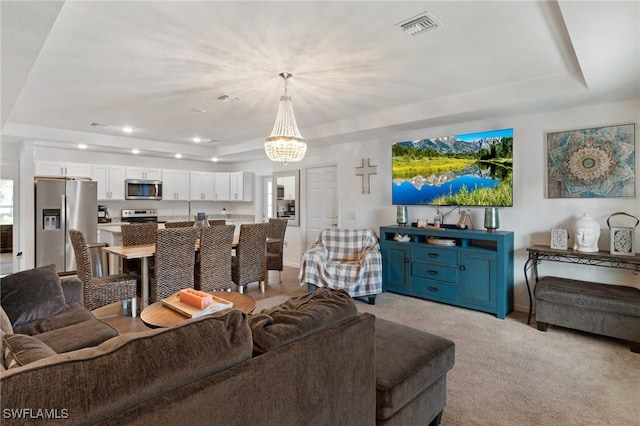 living area with a tray ceiling, recessed lighting, visible vents, and light colored carpet