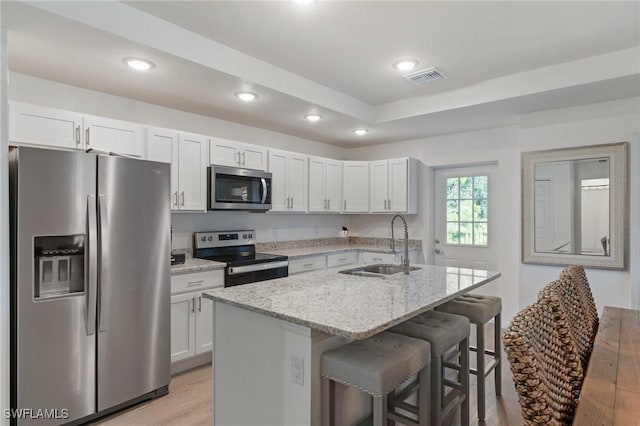 kitchen featuring a sink, visible vents, a kitchen breakfast bar, appliances with stainless steel finishes, and light stone countertops