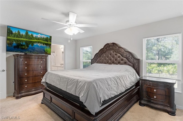 bedroom with a ceiling fan, baseboards, light colored carpet, and ensuite bath