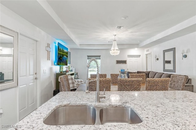 kitchen featuring visible vents, open floor plan, hanging light fixtures, light stone countertops, and a sink