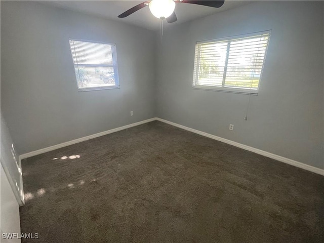 spare room with dark colored carpet, a ceiling fan, and baseboards