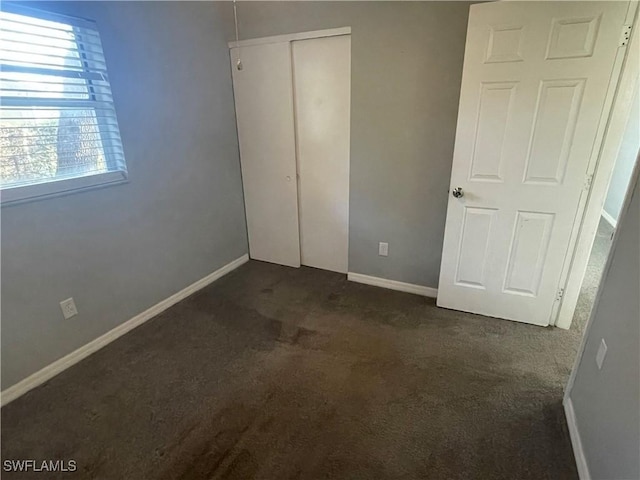 unfurnished bedroom featuring dark colored carpet, a closet, and baseboards