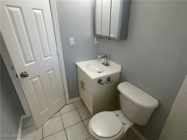 half bath with toilet, vanity, baseboards, and tile patterned floors