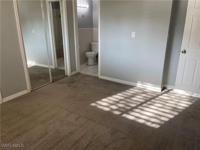 unfurnished bedroom with carpet floors, tile patterned floors, tile walls, and ensuite bathroom