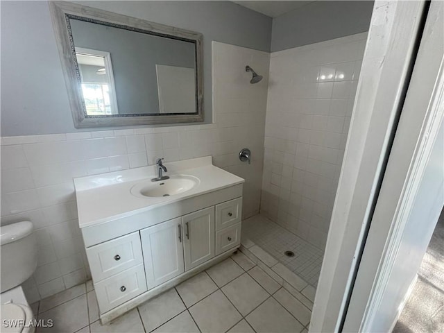 bathroom with toilet, vanity, tile walls, tiled shower, and tile patterned floors