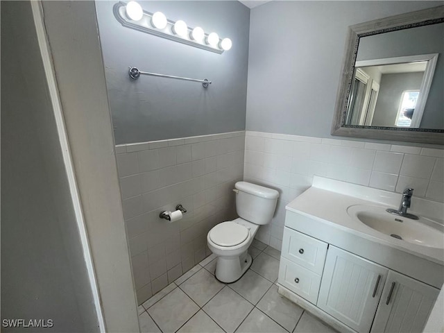 bathroom featuring tile walls, toilet, wainscoting, vanity, and tile patterned floors