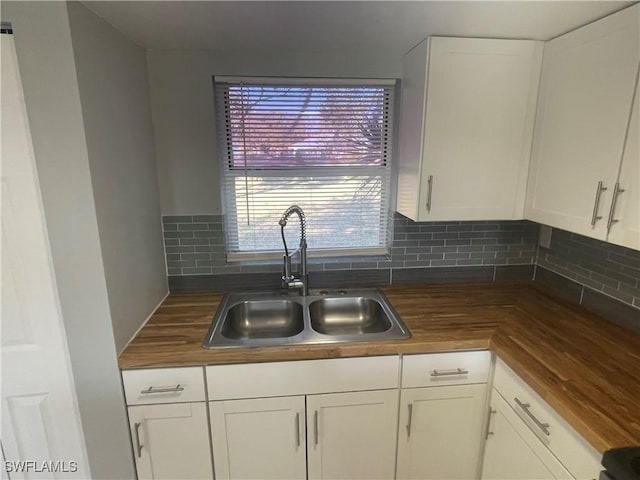 kitchen featuring tasteful backsplash, butcher block countertops, white cabinets, and a sink