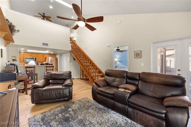 living room with stairway, light wood-type flooring, a ceiling fan, and a towering ceiling