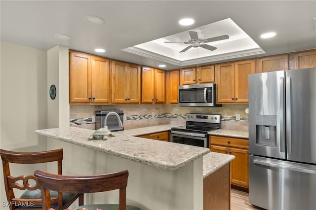 kitchen with tasteful backsplash, stainless steel appliances, a peninsula, a kitchen breakfast bar, and a tray ceiling
