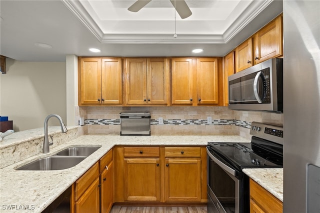 kitchen featuring a sink, stainless steel appliances, decorative backsplash, a raised ceiling, and light stone counters