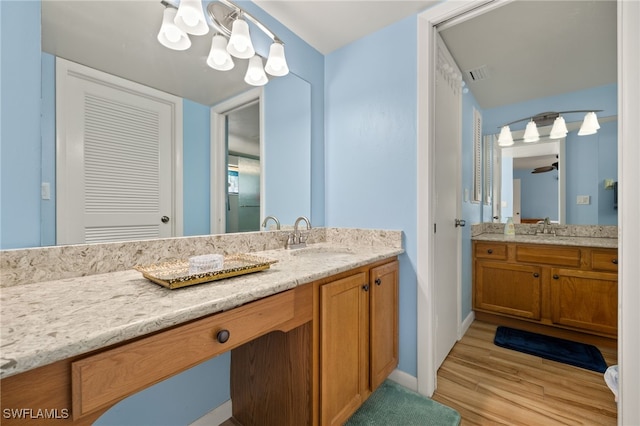 bathroom featuring visible vents, two vanities, wood finished floors, and a sink