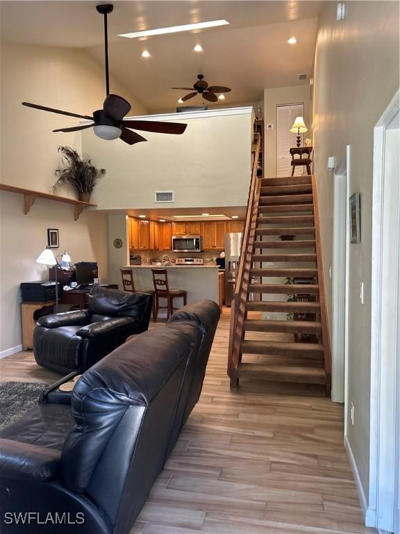 living area featuring stairs, light wood-type flooring, baseboards, visible vents, and a ceiling fan
