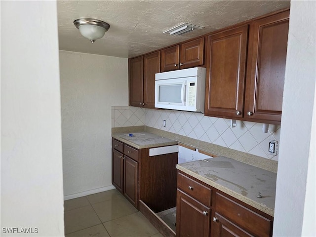 kitchen with light stone counters, light tile patterned floors, decorative backsplash, white microwave, and a textured ceiling