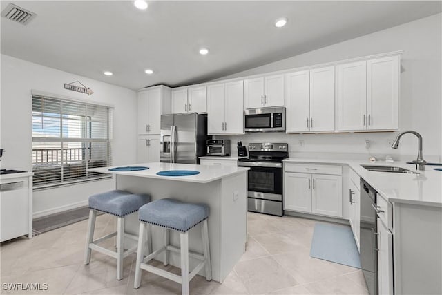 kitchen featuring vaulted ceiling, a kitchen breakfast bar, white cabinets, stainless steel appliances, and a sink