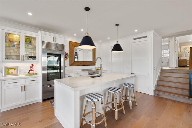 kitchen with light wood finished floors, white cabinets, a sink, stainless steel built in refrigerator, and backsplash