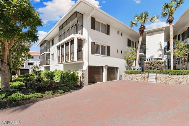 view of side of home with decorative driveway, an attached garage, and stucco siding