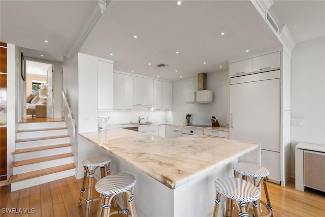 kitchen with paneled built in fridge, a kitchen bar, a peninsula, and white cabinetry