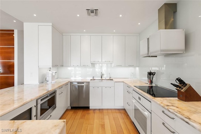 kitchen featuring visible vents, white cabinets, stainless steel appliances, wall chimney range hood, and a sink