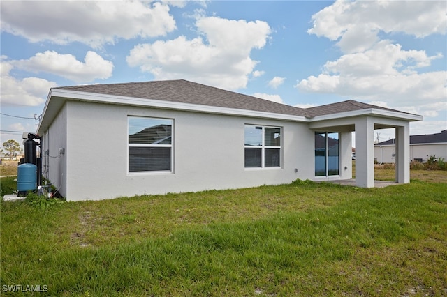 back of house featuring stucco siding, a shingled roof, and a yard