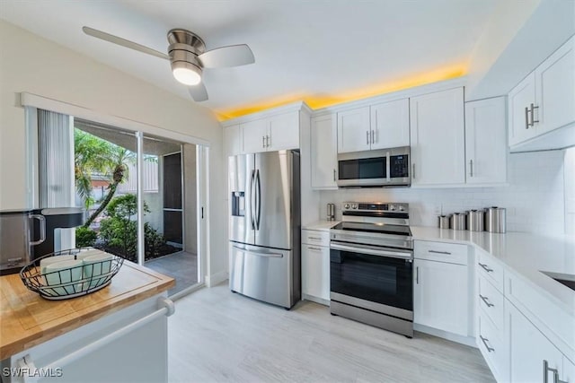 kitchen featuring light wood-style flooring, a ceiling fan, white cabinetry, appliances with stainless steel finishes, and decorative backsplash