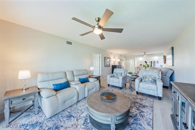 living area featuring light wood-type flooring, visible vents, and ceiling fan