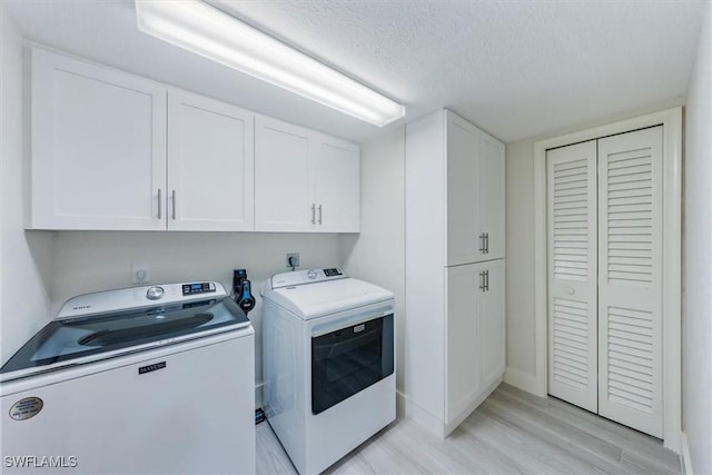laundry room featuring a textured ceiling, separate washer and dryer, light wood-style flooring, and cabinet space