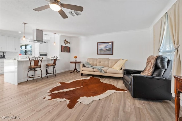 living area featuring light wood-type flooring, visible vents, crown molding, baseboards, and ceiling fan