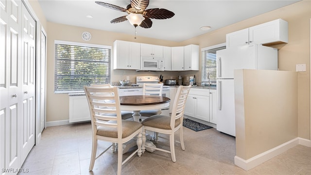 kitchen featuring baseboards, white appliances, plenty of natural light, and white cabinets