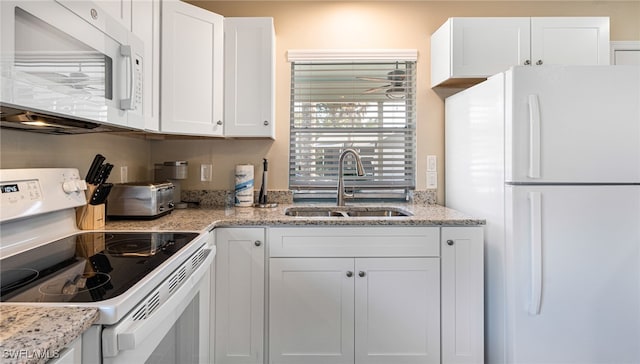 kitchen with a toaster, white cabinetry, a sink, light stone countertops, and white appliances