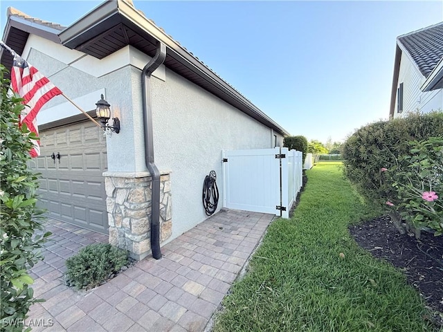 view of side of property with a garage, fence, stone siding, a lawn, and stucco siding