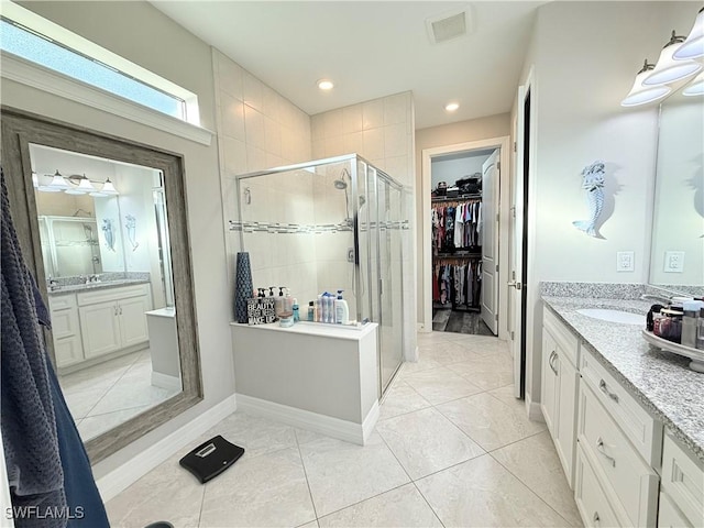 bathroom with two vanities, visible vents, tile patterned floors, a stall shower, and a walk in closet