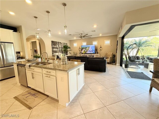 kitchen with a ceiling fan, light stone counters, open floor plan, stainless steel appliances, and a sink