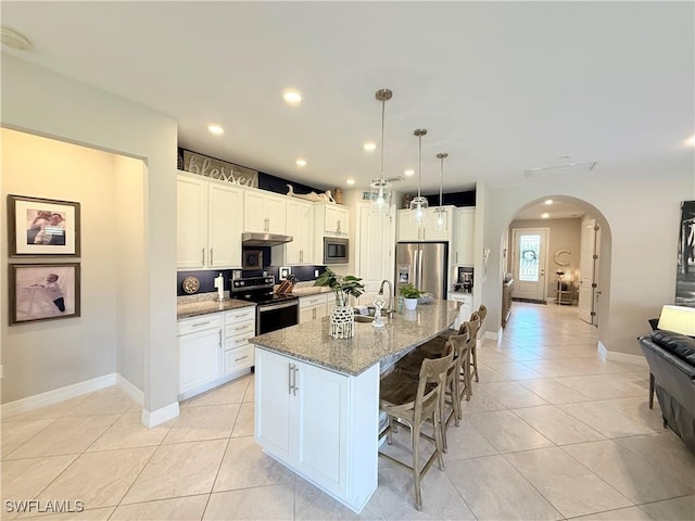 kitchen with arched walkways, a breakfast bar area, appliances with stainless steel finishes, light stone counters, and light tile patterned flooring