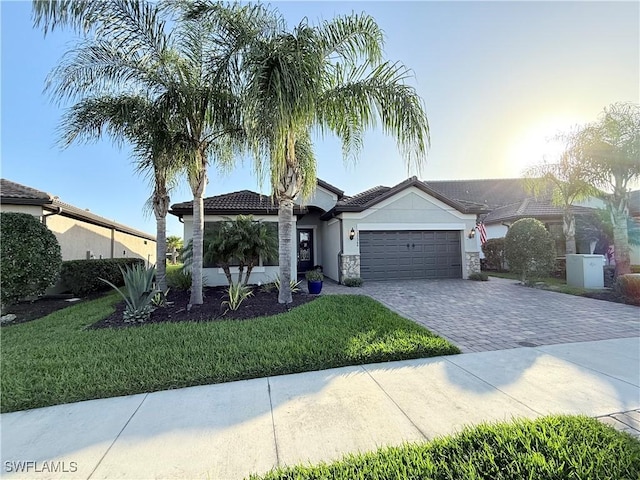 view of front of house featuring decorative driveway, stucco siding, an attached garage, a front yard, and stone siding