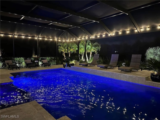 pool at night with glass enclosure, a patio area, and an outdoor pool