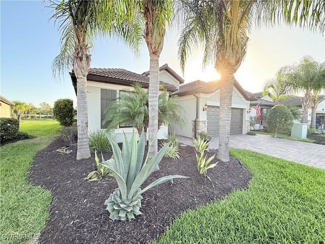 mediterranean / spanish home with a garage, a tile roof, decorative driveway, stucco siding, and a front lawn