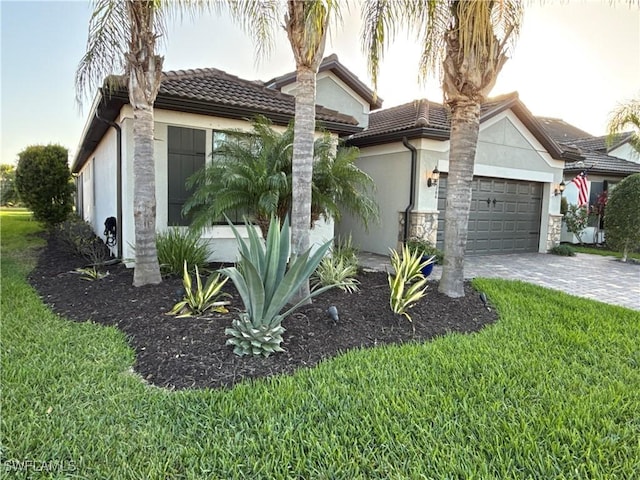 view of front of house featuring an attached garage, a tiled roof, decorative driveway, stucco siding, and a front yard