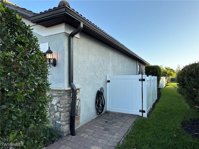 view of side of home with a yard, stone siding, fence, and stucco siding