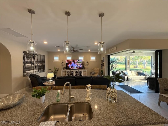 kitchen with stone counters, a sink, open floor plan, tile patterned floors, and decorative light fixtures