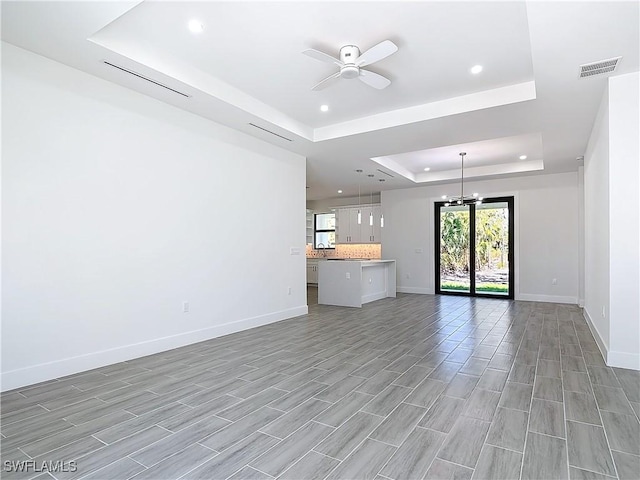 unfurnished living room featuring baseboards, visible vents, a raised ceiling, ceiling fan with notable chandelier, and recessed lighting