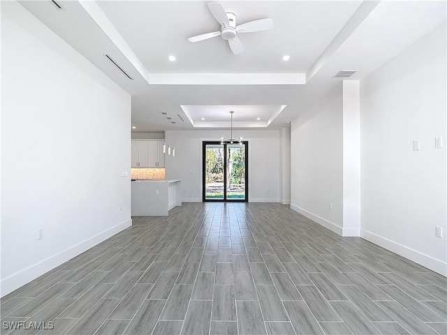 unfurnished living room with baseboards, visible vents, a raised ceiling, ceiling fan with notable chandelier, and recessed lighting